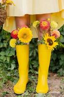 Feet in yellow rubber boots with autumn flowers near the vineyard photo