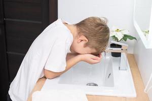 The cute boy leaned over to the sink to wash his face photo