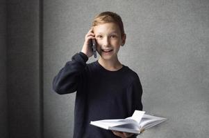 A happy boy is holding a book in his hands and talking on the phone photo