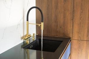 Water pours from the black and gold faucet in the kitchen into the sink photo