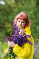 A cute teenage girl with pink hair and a bouquet of lupines is standing in a yellow raincoat photo