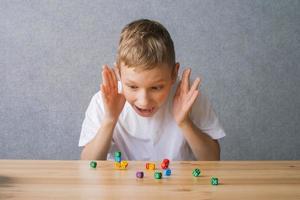 Cute boy plays with multicolored playing dice for board game, builds a tower up photo