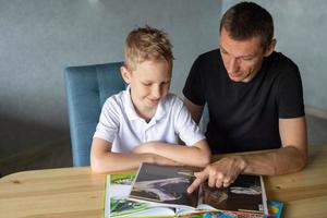 un linda chico es sentado a el mesa con su papá y acecho un libro acerca de serpientes foto