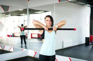 un atlético niña soportes en el gimnasio y muestra ejercicios para grupo aptitud con un aptitud bar foto