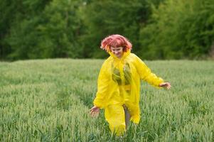 un joven niña en un amarillo impermeable carreras mediante un verde trigo campo foto