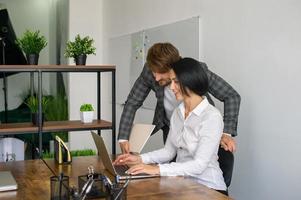 a man and a woman in the office are working at a laptop and smiling photo