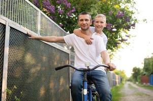 A cute boy in a white T-shirt rides a bike with his dad and laughs. photo