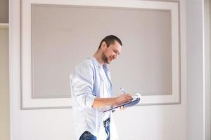 A man in a shirt stands in a room with a folder and takes notes photo
