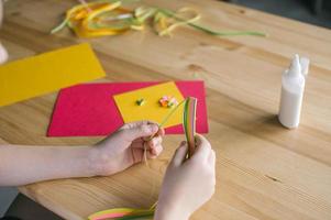 el niño manos hacer un tarjeta fuera de encañonado, largo estrecho de colores tiras de encañonado papel foto