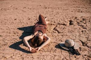 A young girl in a dress and with a hat is lying on the sand photo