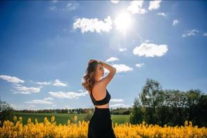 a girl in a black top and black trousers stands in a yellow rapeseed field in spring photo