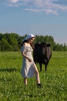 un joven niña va a un vaca pasto en un vestido. agrícola industria foto