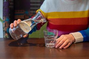 un persona con Alzheimer enfermedad intentos a verter agua dentro un vaso. verter agua en el mesa foto