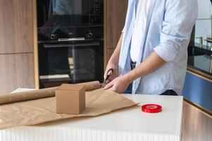 un hombre en pie a un mesa cortes apagado papel para regalo envase con tijeras foto