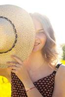 The girl smiles and holds a straw hat near her face in the rays of the sun photo