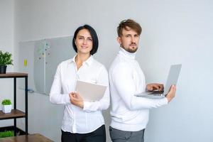 Portrait of a man with a laptop and a woman with a notebook standing in an office in white clothes photo