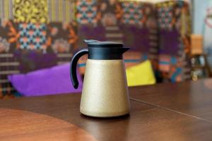 A golden teapot with a black lid stands on the table photo