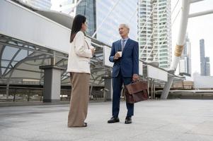 Asian senior mature middle aged businessman and young businesswoman having a discussion and coffee in modern city photo