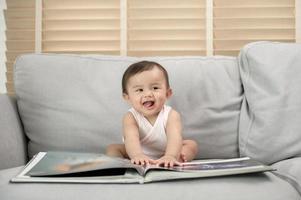 bebé niña leyendo un libro sentado en sofá a hogar foto