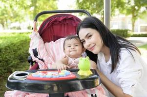 Beautiful mom with a baby girl sitting on baby trolley outdoor in sunshine day photo