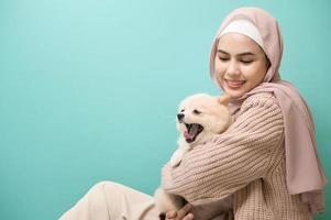Portrait of Young muslim woman kisses and hugs her dog over green background. photo