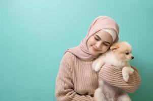 Portrait of Young muslim woman kisses and hugs her dog over green background. photo