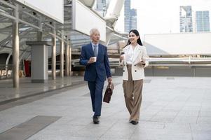 Asian senior mature middle aged businessman and young businesswoman having a discussion and coffee in modern city photo