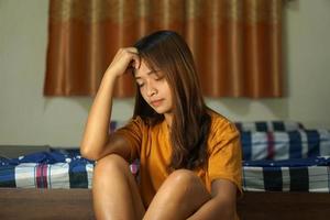 asiático mujer lucha desde trabajo sentar junto a el cama foto