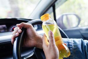 Asian woman driver hold cold water for drink in car, dangerous and risk an accident. photo