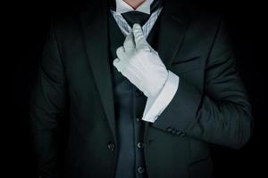 Isolated Close-Up of Butler or Concierge in Dark Suit and White Gloves Straightening Tie. Service Industry and Professional Hospitality. photo