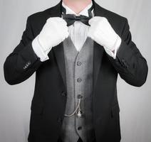 Portrait of Butler in Dark Formal Suit and White Gloves Straightening Bow Tie. Service Industry and Professional Hospitality. photo