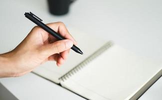 left handed man holding a pen and writing in a notebook on the table photo