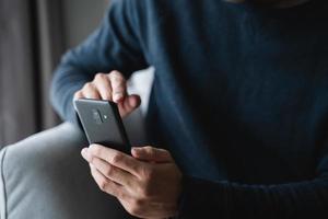 man using smartphone on sofa in living room at home, searching data and social media on internet. photo