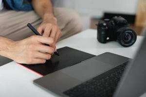 hombre diseñador utilizando bolígrafo ratón tableta dibujo y escritura en tableta tablero con aguja para retocando, y gráfico diseño. foto