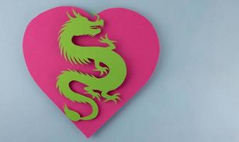 A green paper dragon lies on a pink heart on a blue background. The concept of the new year 2024 photo