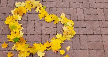 Heart of autumn yellow maple leaves on the red garden path photo