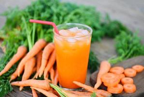 jugo de zanahoria en el fondo de la mesa de madera, rodajas de zanahoria frescas y dulces para cocinar frutas y verduras para el concepto de salud, jugo de zanahoria fresco en vidrio con hielo en verano foto