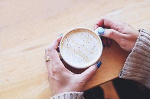 coffee caramel woman coffee with hand holding a cup on the wood table, caramel coffee cup in the morning - hot caramel macchiato - top view photo