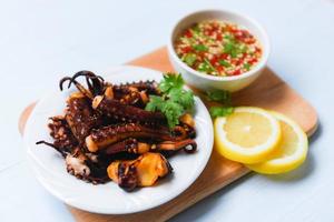 octopus salad with lemon herbs and spices on white plate - Tentacles squid grilled appetizer food hot and spicy chilli sauce seafood cooked served on wooden cutting board in the restaurant photo