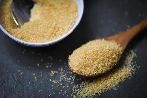 brown sugar in wooden spoon on dark black background with cane sugar on white bowl photo