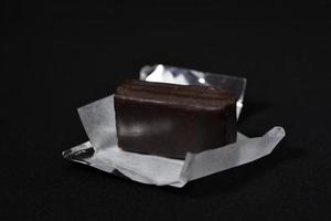 Chocolate candy in a package on a black background. Sweet candy. A chocolate bar in a paper package. photo