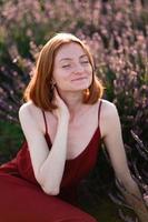 A red-haired young girl without make-up is resting in a lavender field. Summer vacation and travel time. photo