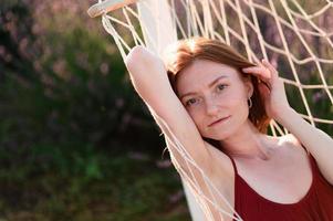 A red-haired young girl without make-up is resting in a lavender field. Summer vacation and travel time. photo