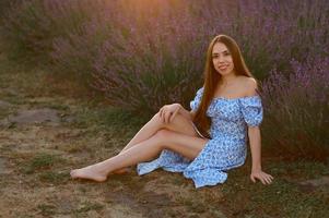 atractivo esbelto contento niña en un azul vestir en un lavanda campo a puesta de sol. foto