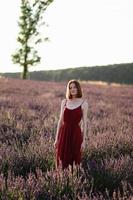 A red-haired young girl without make-up is resting in a lavender field. Summer vacation and travel time. photo