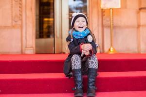 Little girl sitting on red carpet stairs photo