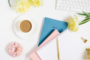 Notebook for daily planning with breakfast serving on a white background, a cup of coffee, a donut, flowers and a gift box with a bow. The concept of daily planning of life, work, study photo