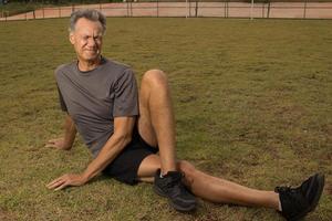 Mature man outside on the grass doing Stretches before working out photo