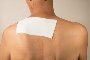 Man wearing a medicated patch for pain relief near his shoulder blade and upper back. photo