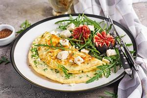 Omelette with feta cheese, parsley and salad with figs, arugula on white plate. Frittata - italian omelet. photo